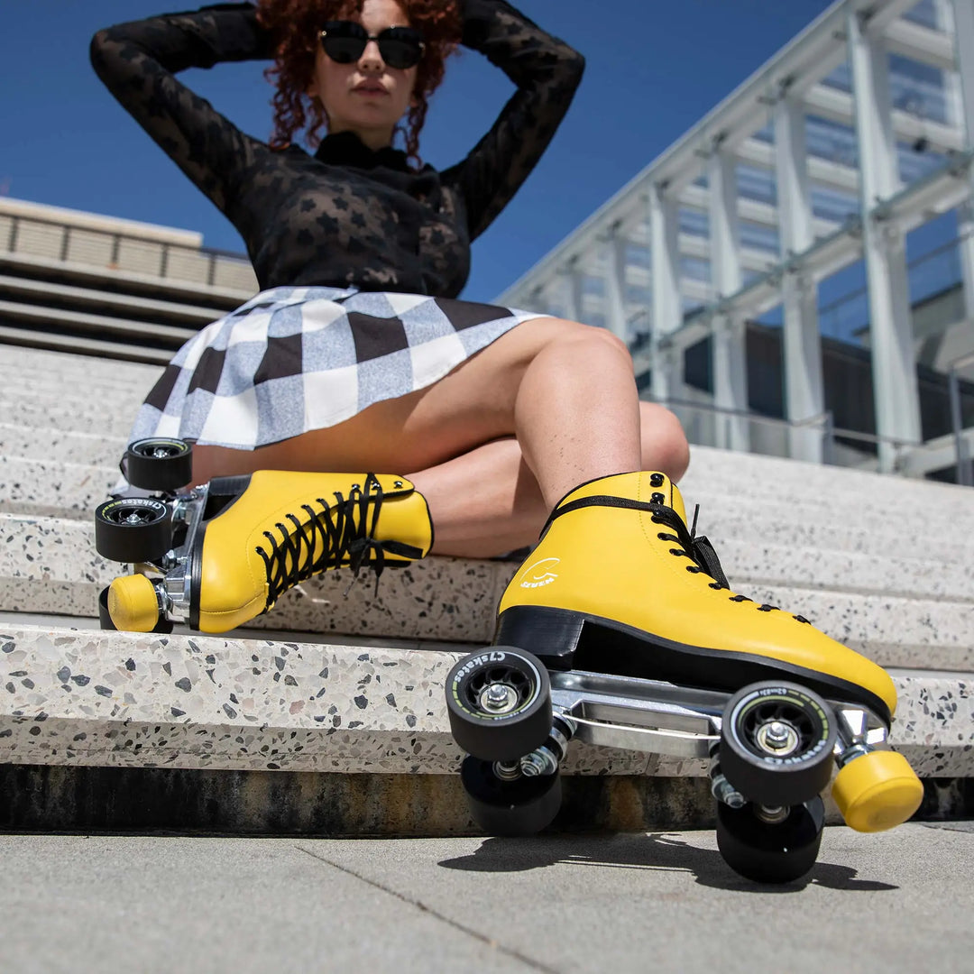 Person wearing yellow roller skates sitting on steps with a modern building in the background