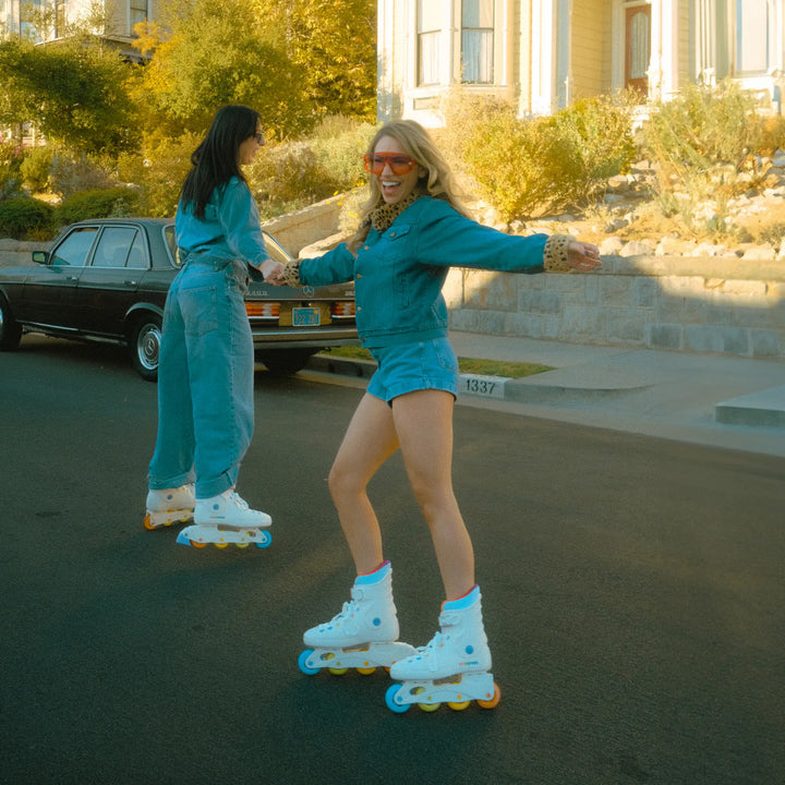 Two women in turquoise outfits and roller skates on a street.