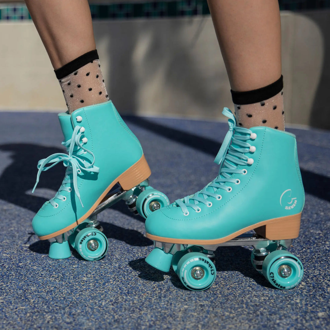 Teal roller skates with wooden soles worn by a person on a concrete surface.