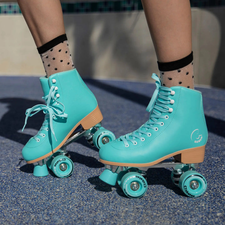 Teal roller skates with wooden soles worn by a person on a concrete surface.