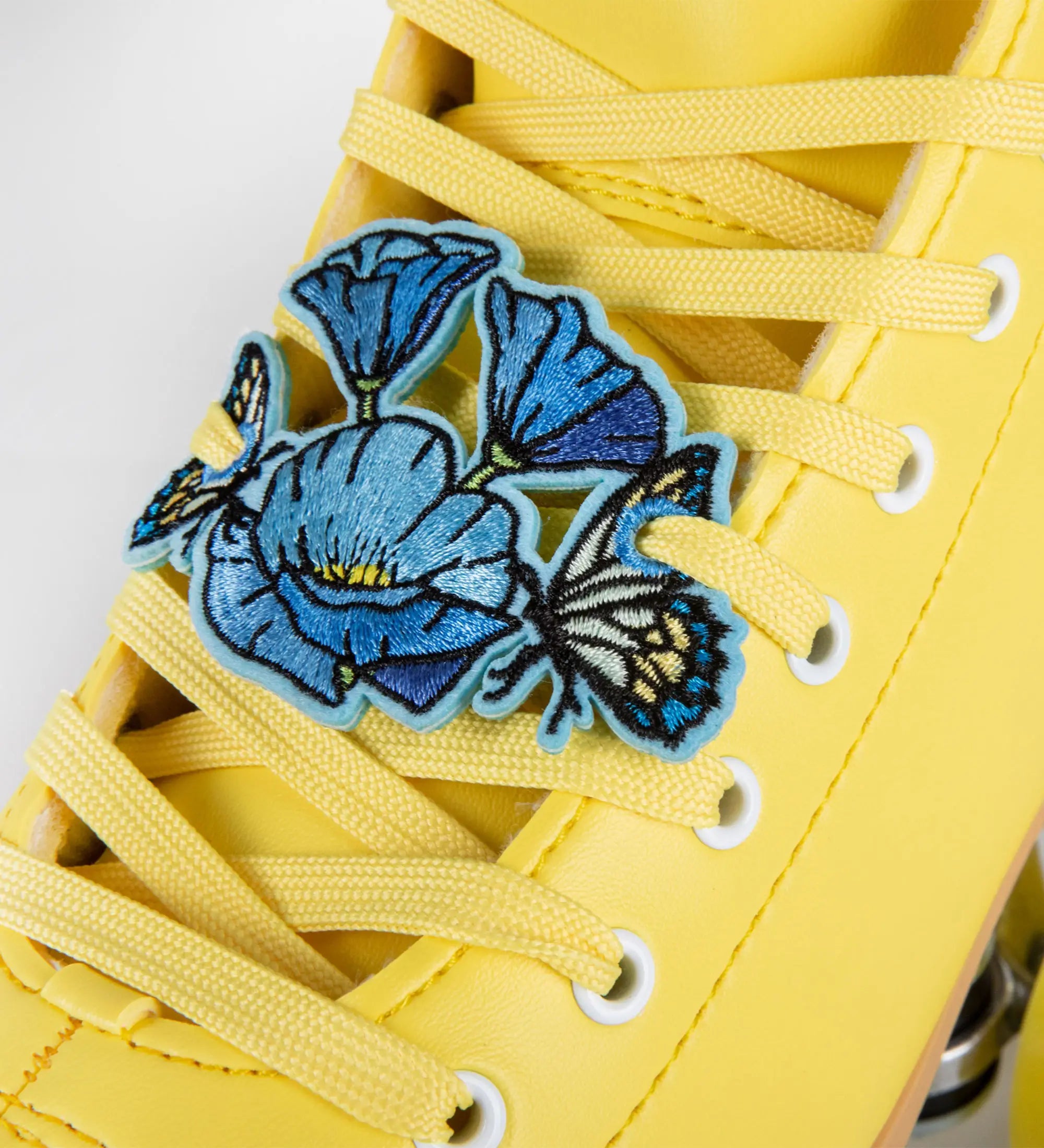 Yellow sneaker with blue floral and butterfly patch on a white background