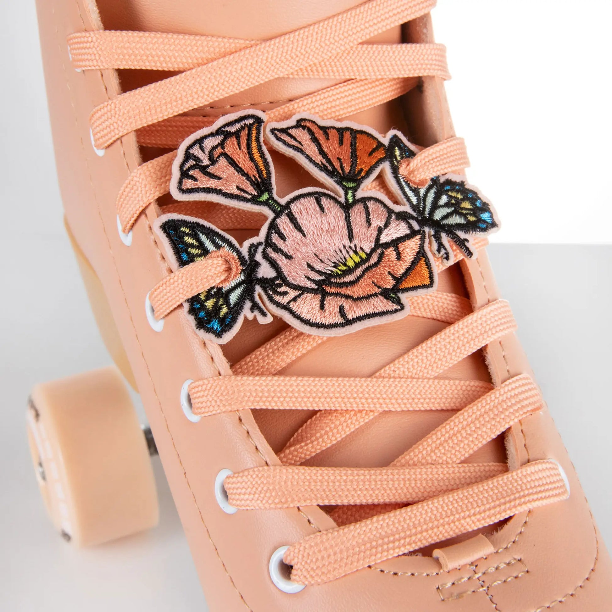 Close-up of a pink sneaker with floral charm and matching laces on a light background