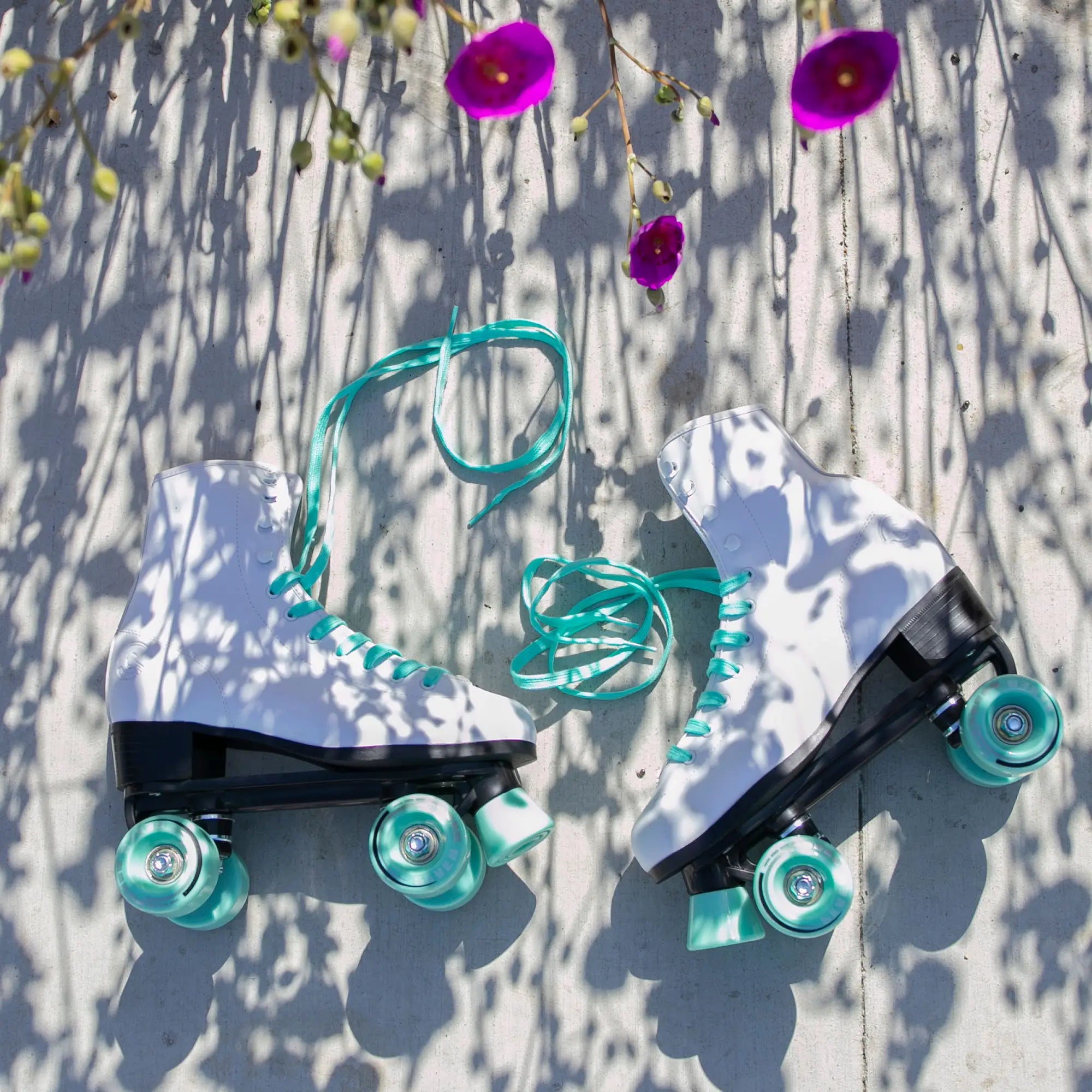 Pair of roller skates with teal laces and wheels on a textured surface with flowers.