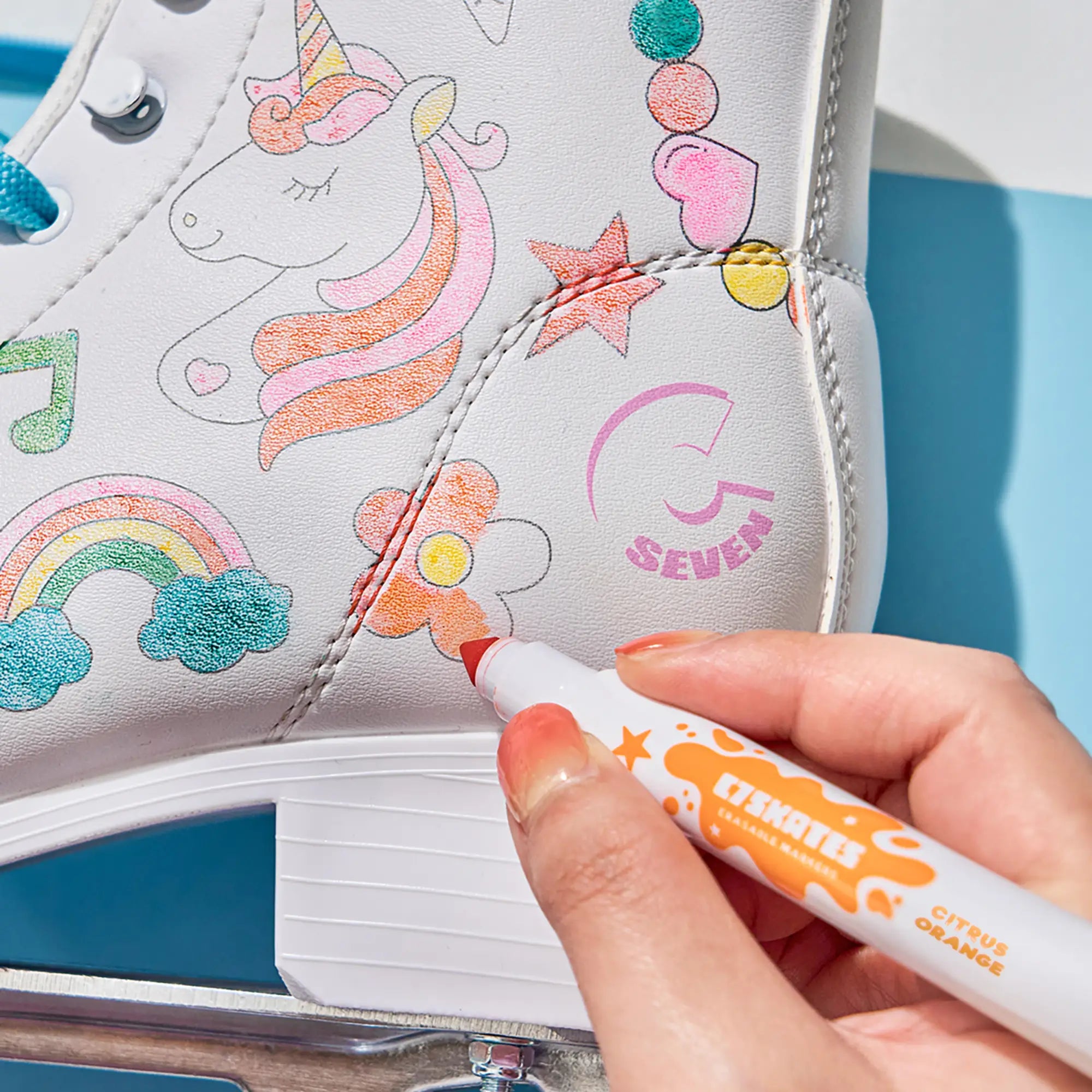 White shoe with colorful designs being decorated with a marker, against a blue background