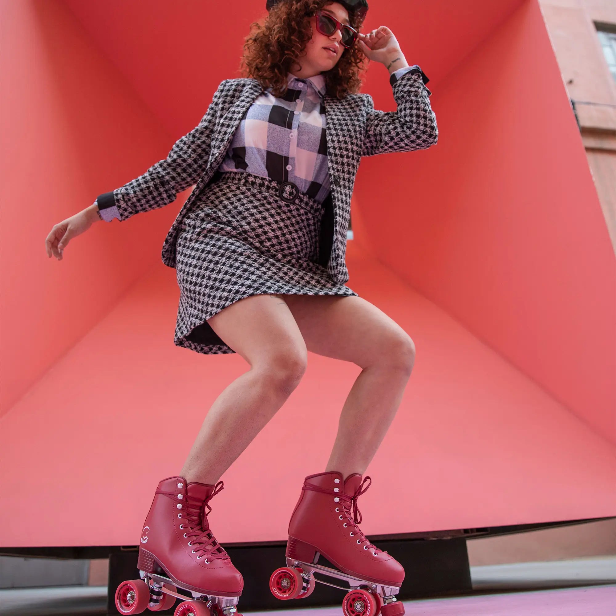 Person wearing a checkered outfit and red roller skates against a pink wall.