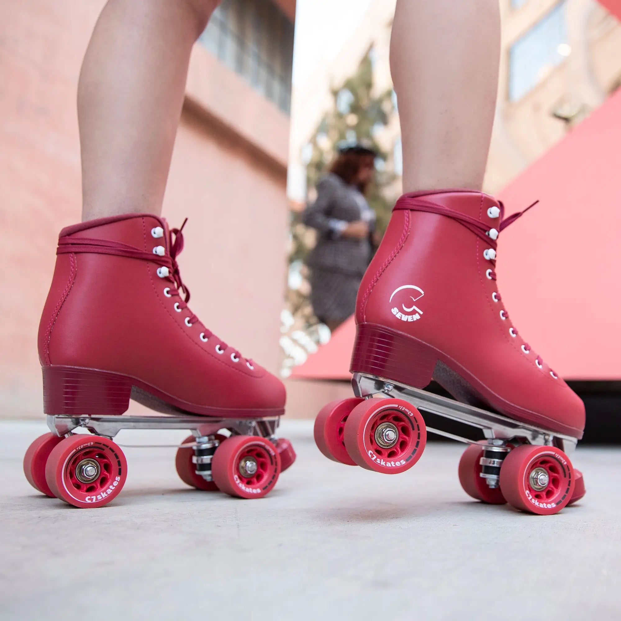 Red roller skates with pink wheels worn by a person on a light surface.