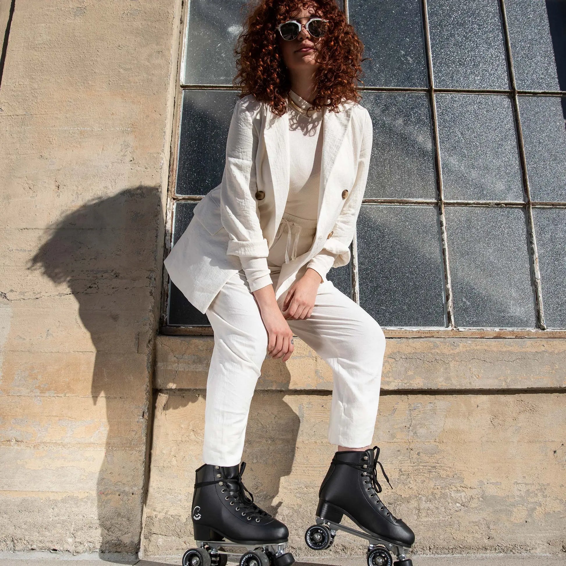 Person wearing a white outfit with roller skates sitting against a stone wall.