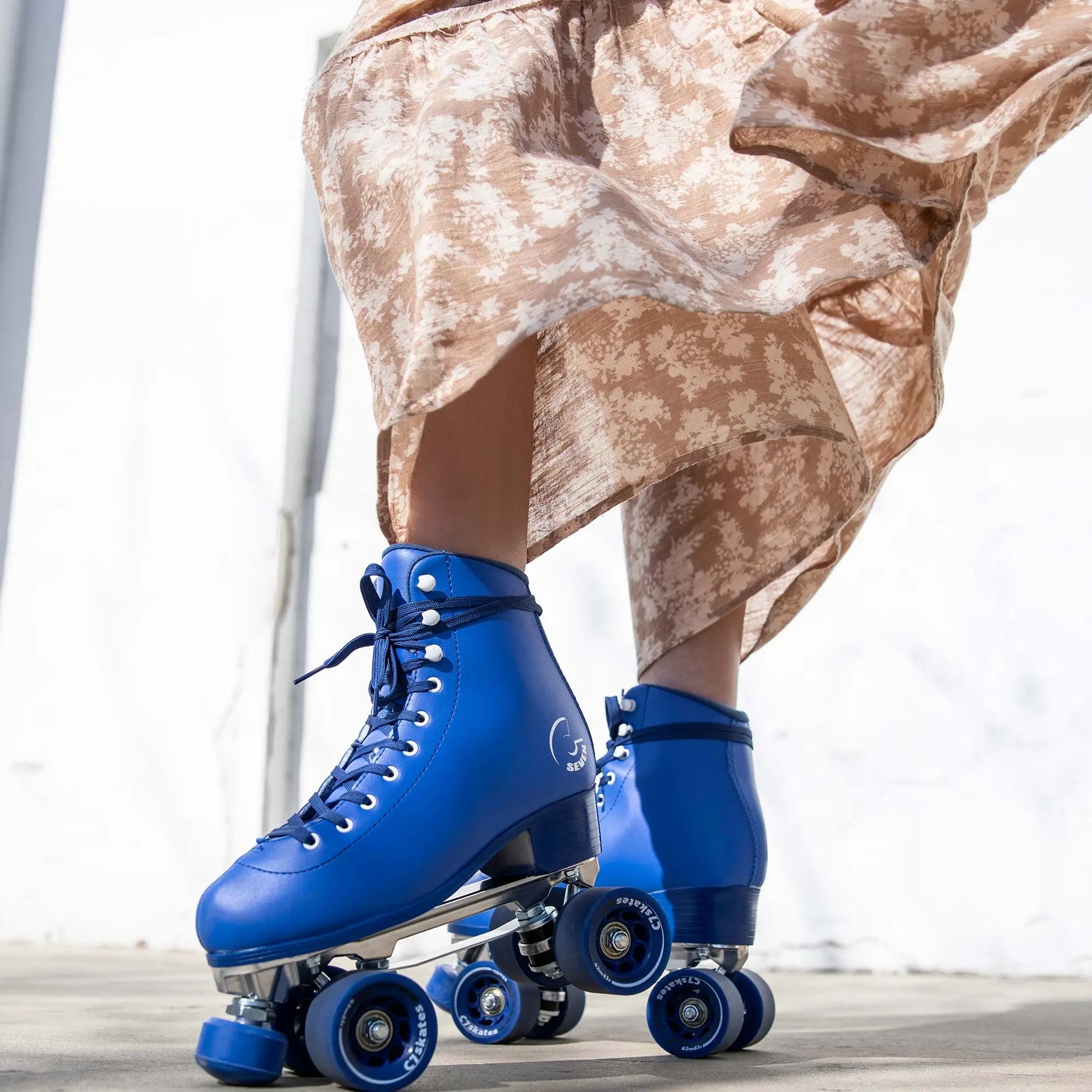 Blue roller skates worn with a patterned skirt on a light background
