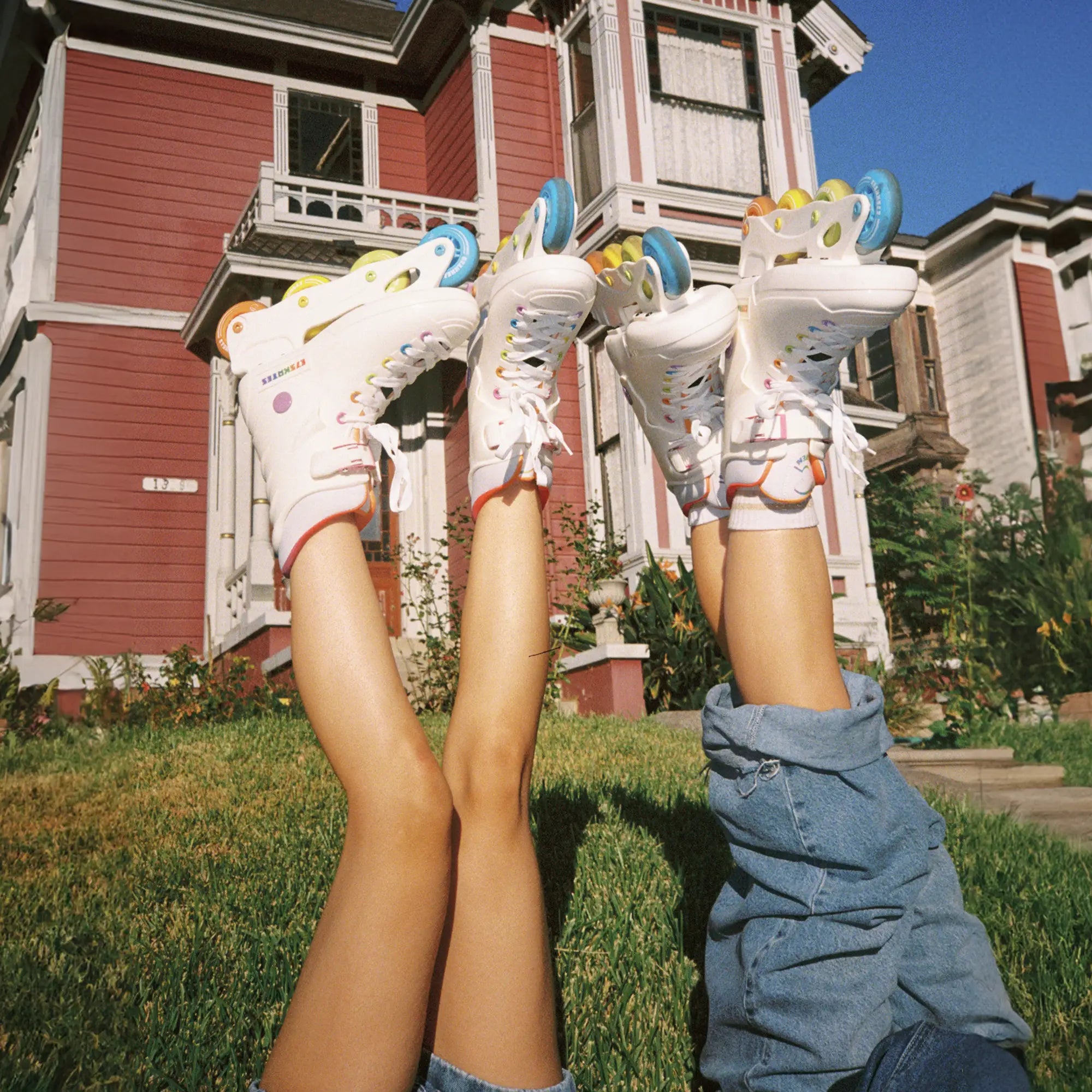 Two pairs of legs wearing roller skates in front of a house.