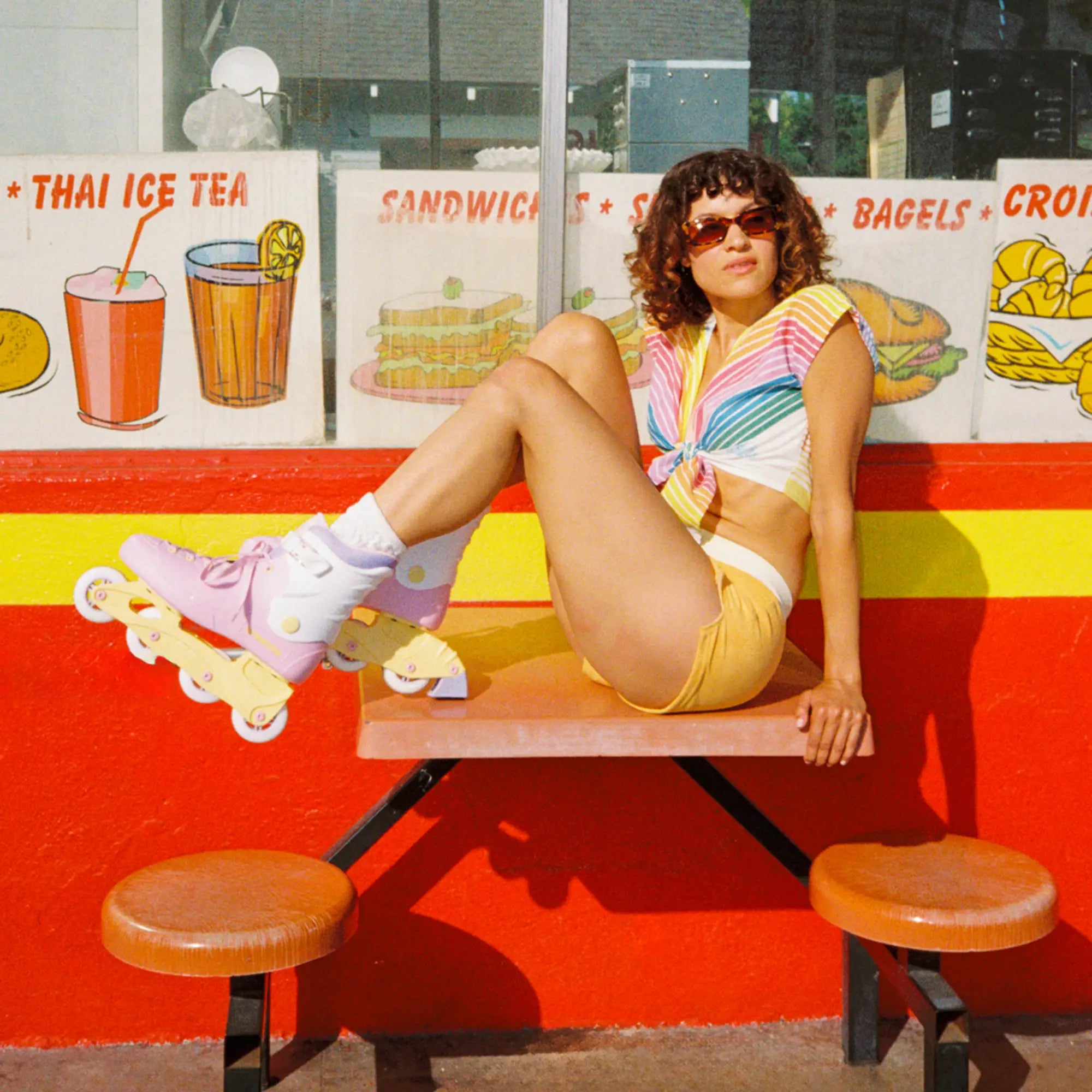 Person sitting on a picnic table with roller skates in front of a colorful wall with food signs.