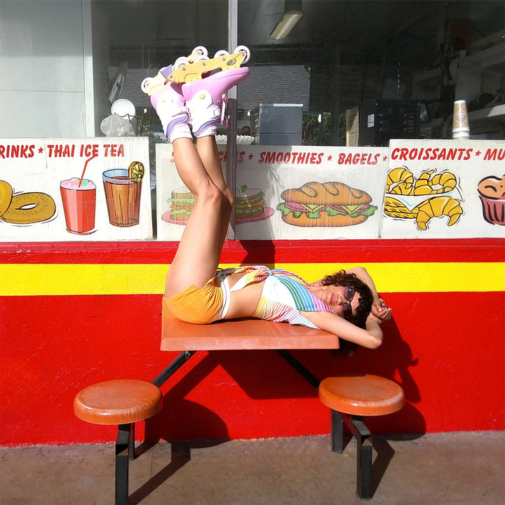 Person lying on a picnic table with colorful shoes in front of a food truck menu.
