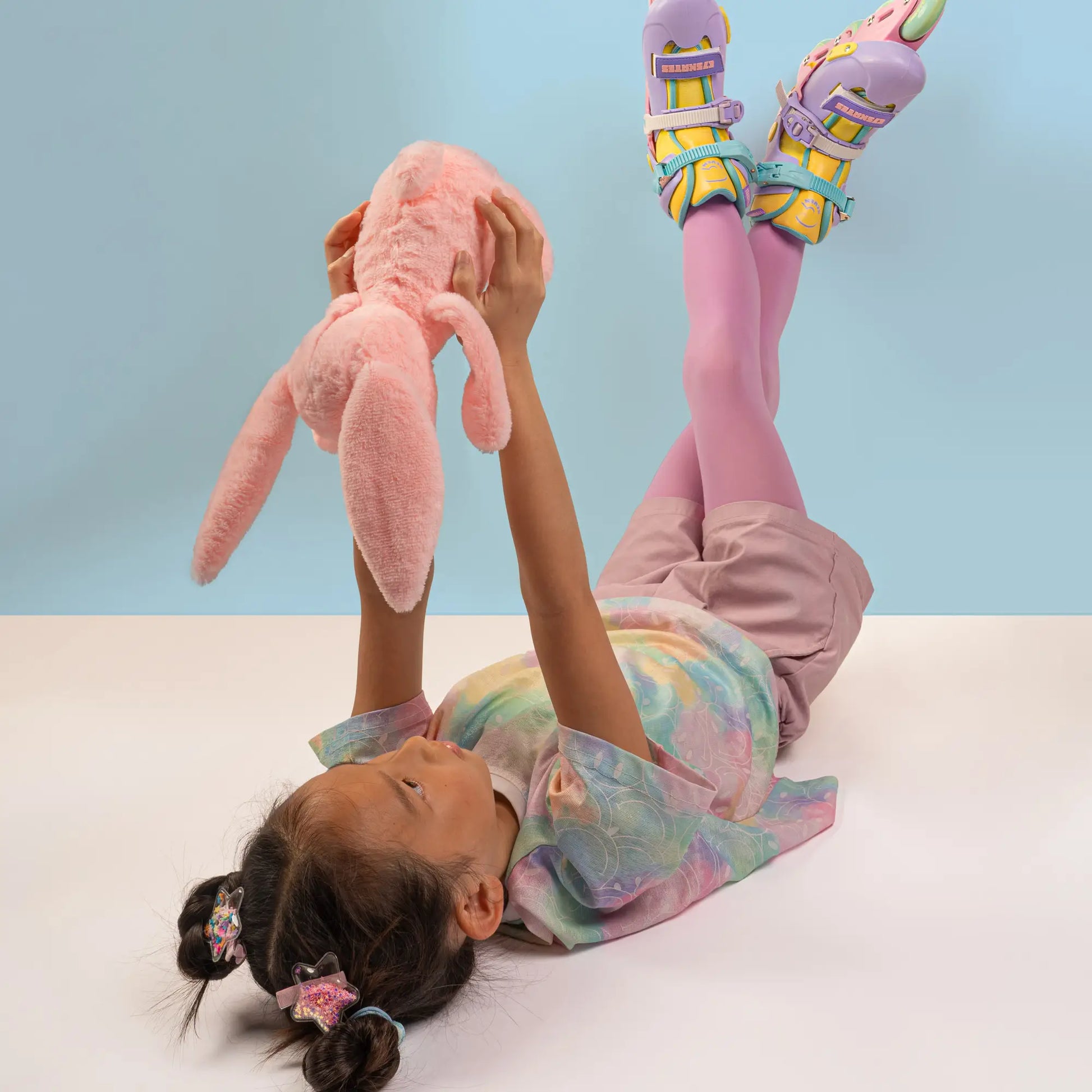 Child playing with a pink stuffed animal on a light blue background