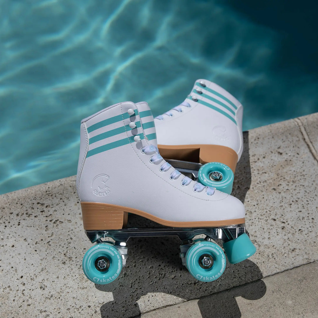 White roller skates with turquoise wheels on a concrete edge by a pool.