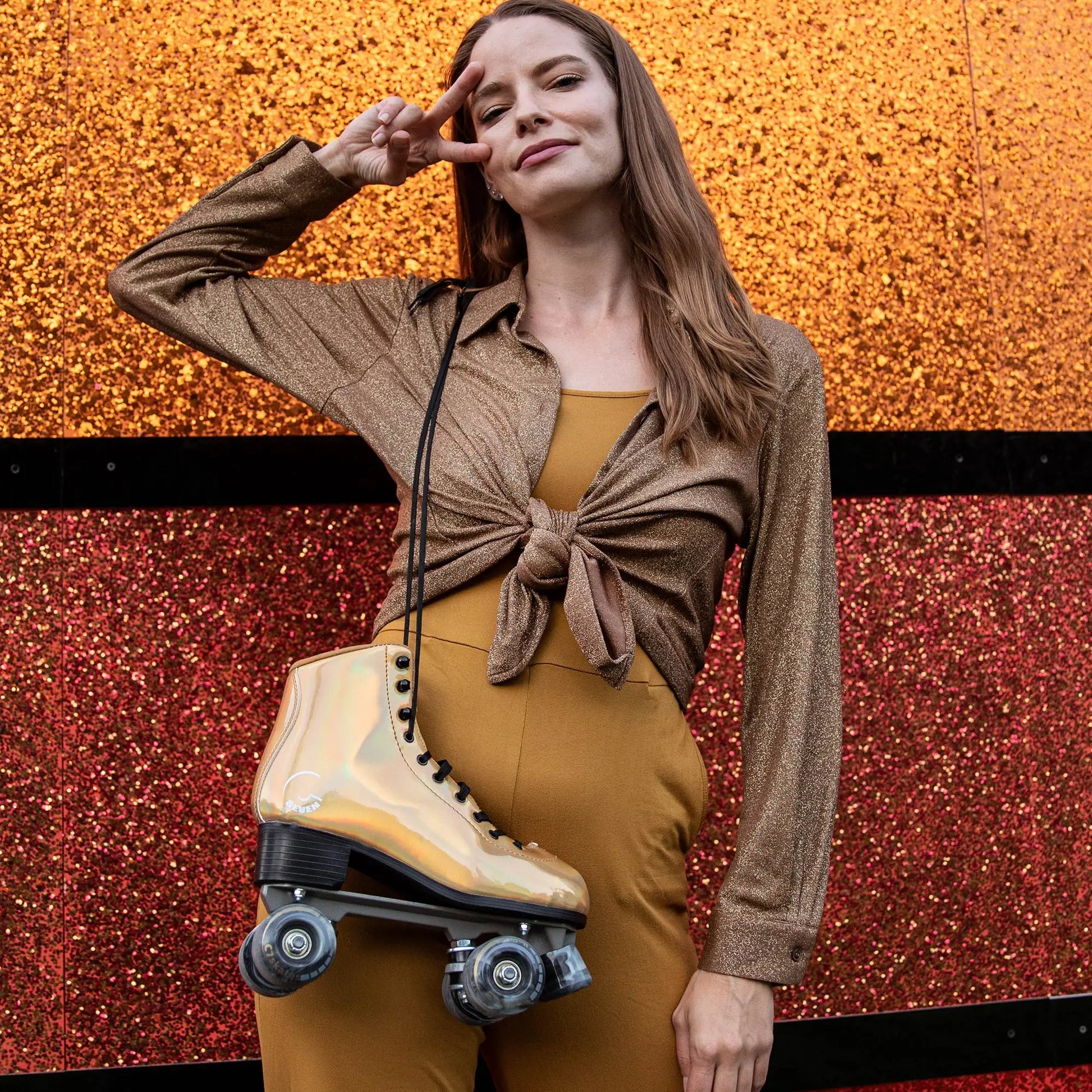 Woman posing with a gold roller shoe against a glittery red and orange background