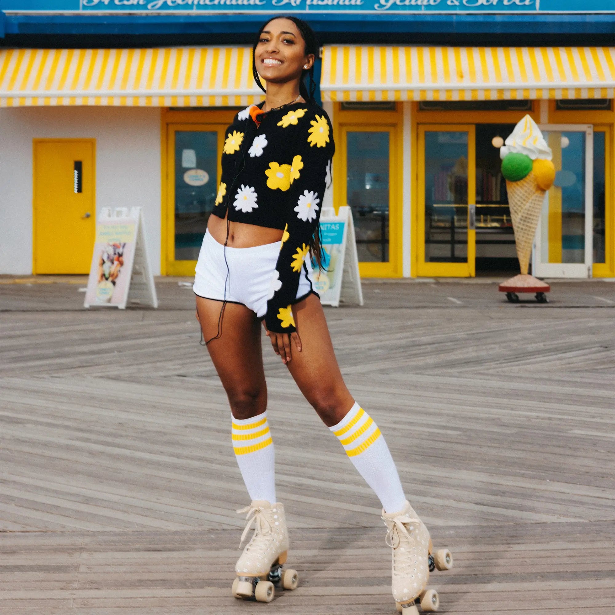 Woman in a black floral sweater and white shorts roller skating on a boardwalk.