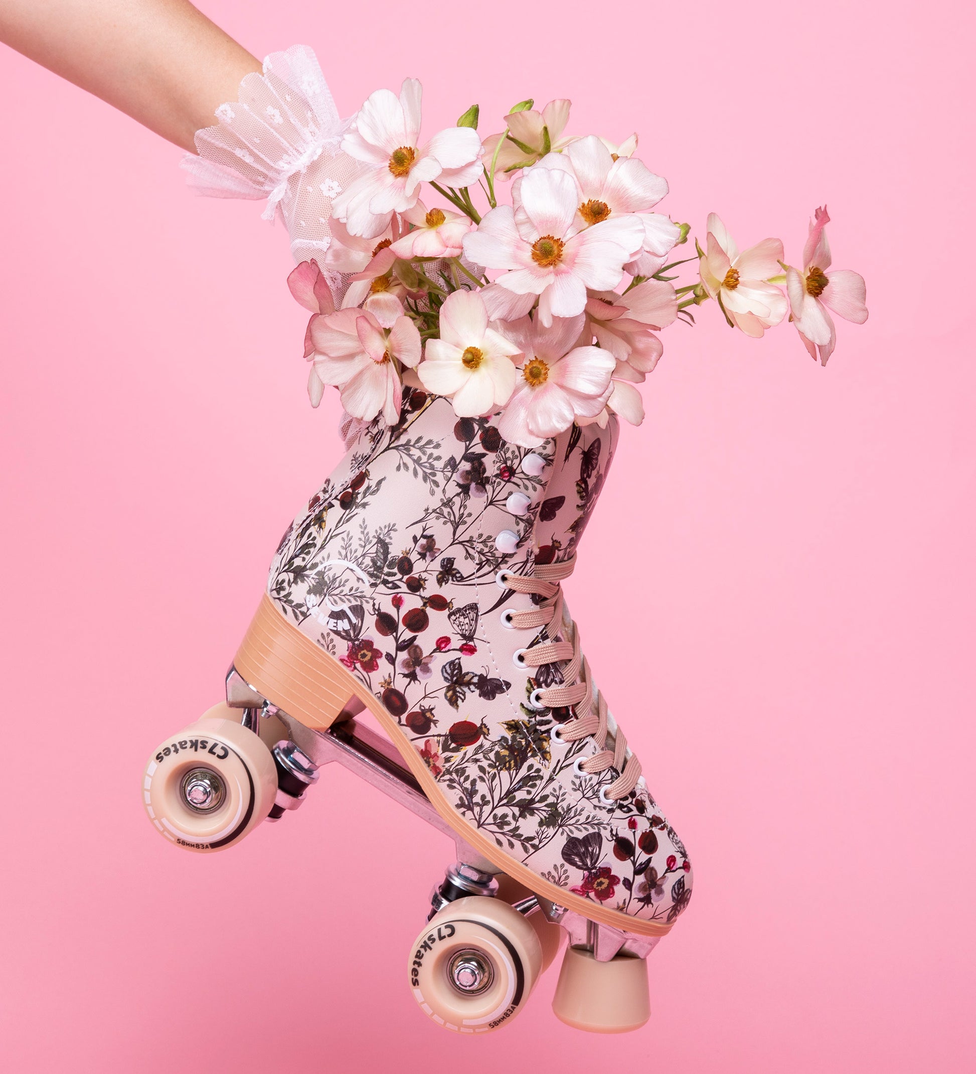 Floral-patterned roller skate held by a hand with white gloves against a pink background