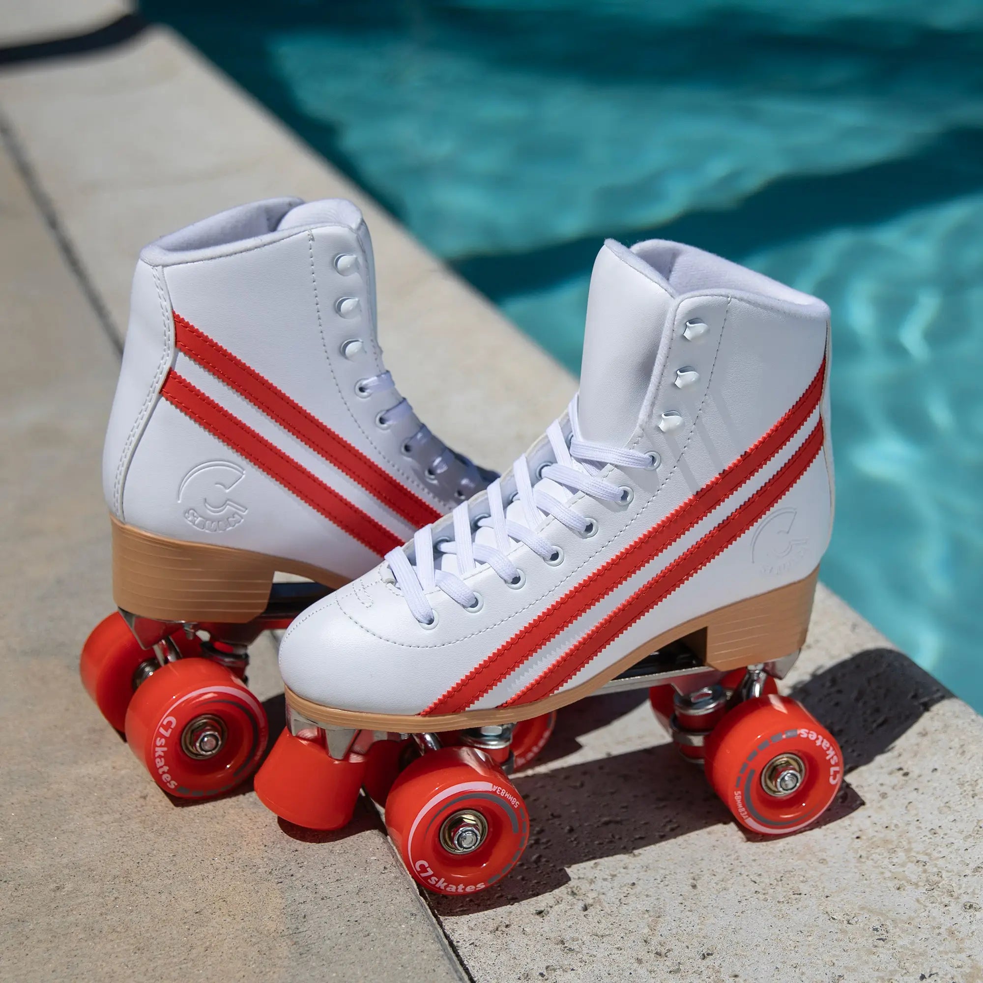 White roller skates with red stripes and red wheels on a concrete surface near a pool.
