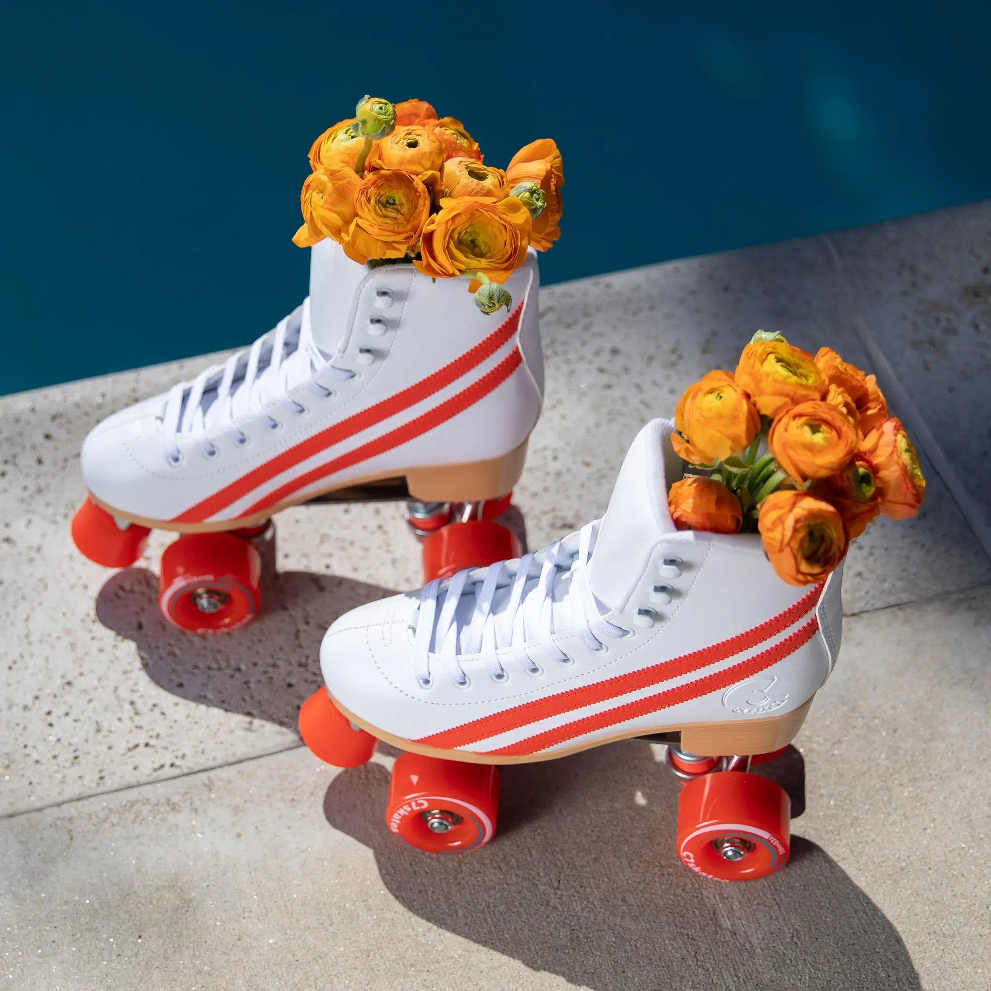 White roller skates with orange flowers on a concrete surface.