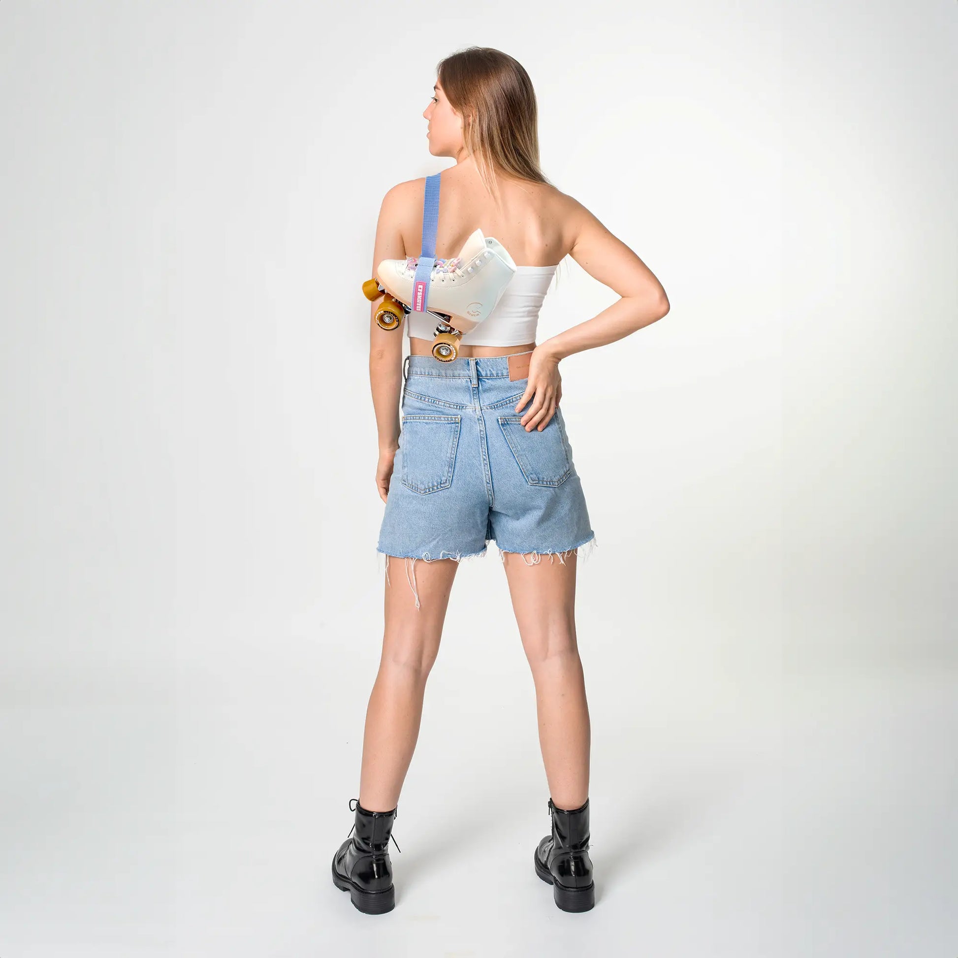 Person wearing a white crop top and blue denim shorts holding a skate roller featuring the brand 'C7Skates' 