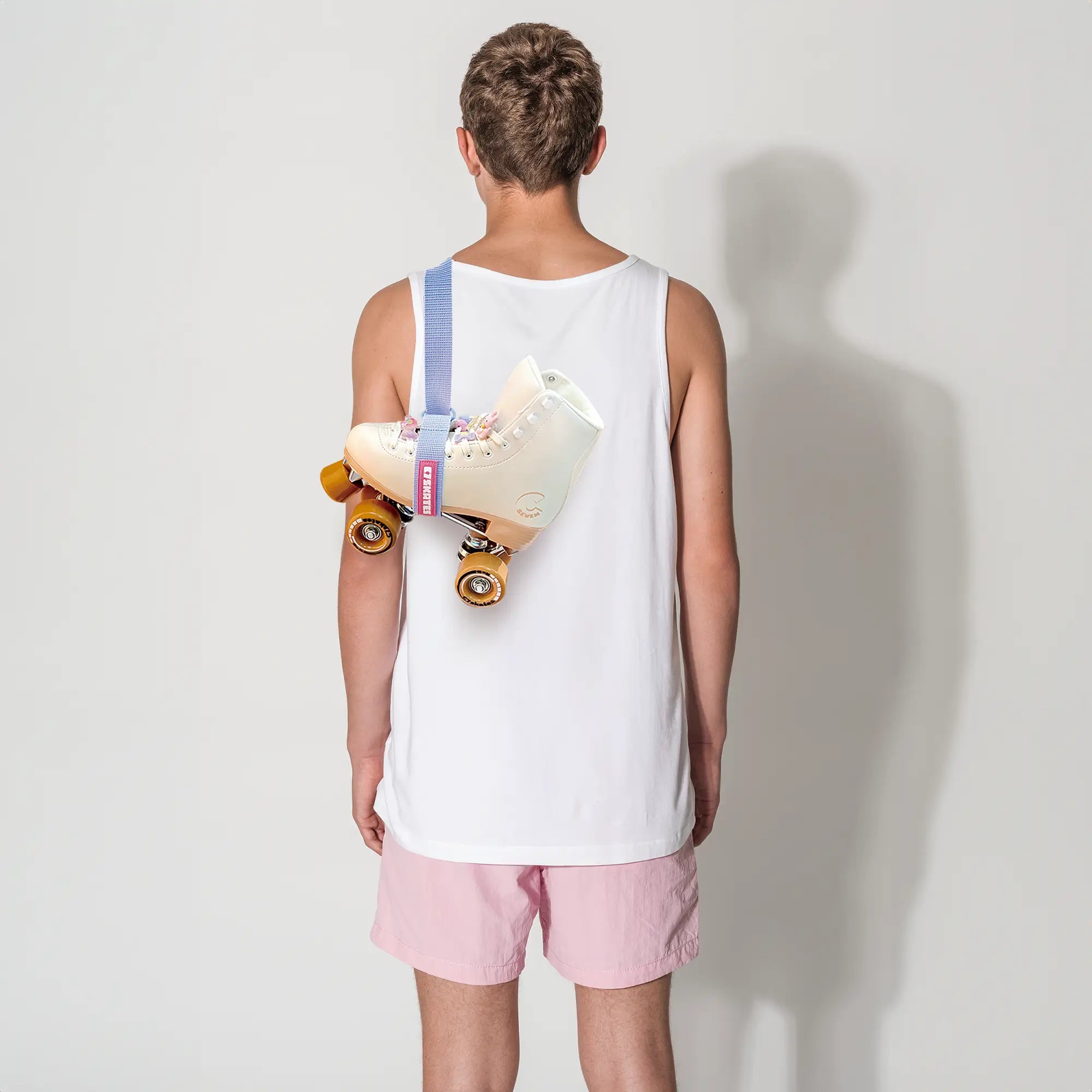 Person wearing a white tank top and pink shorts holding a skate roller with a blue strap with a plain background