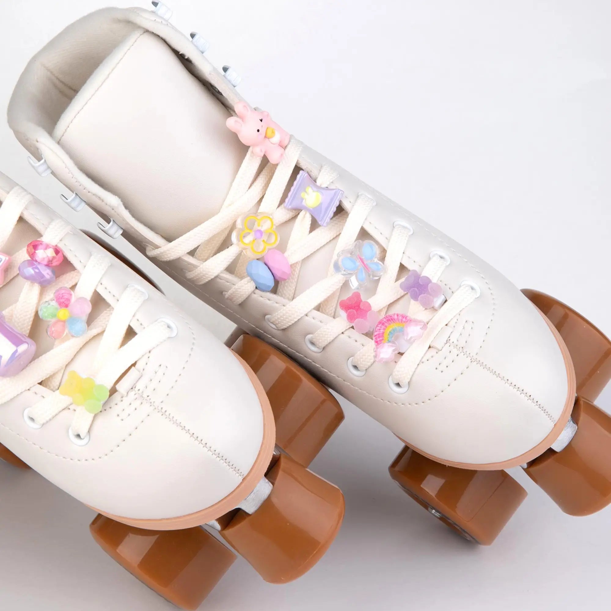 White roller skates with decorative laces charms and brown wheels on a light gray background