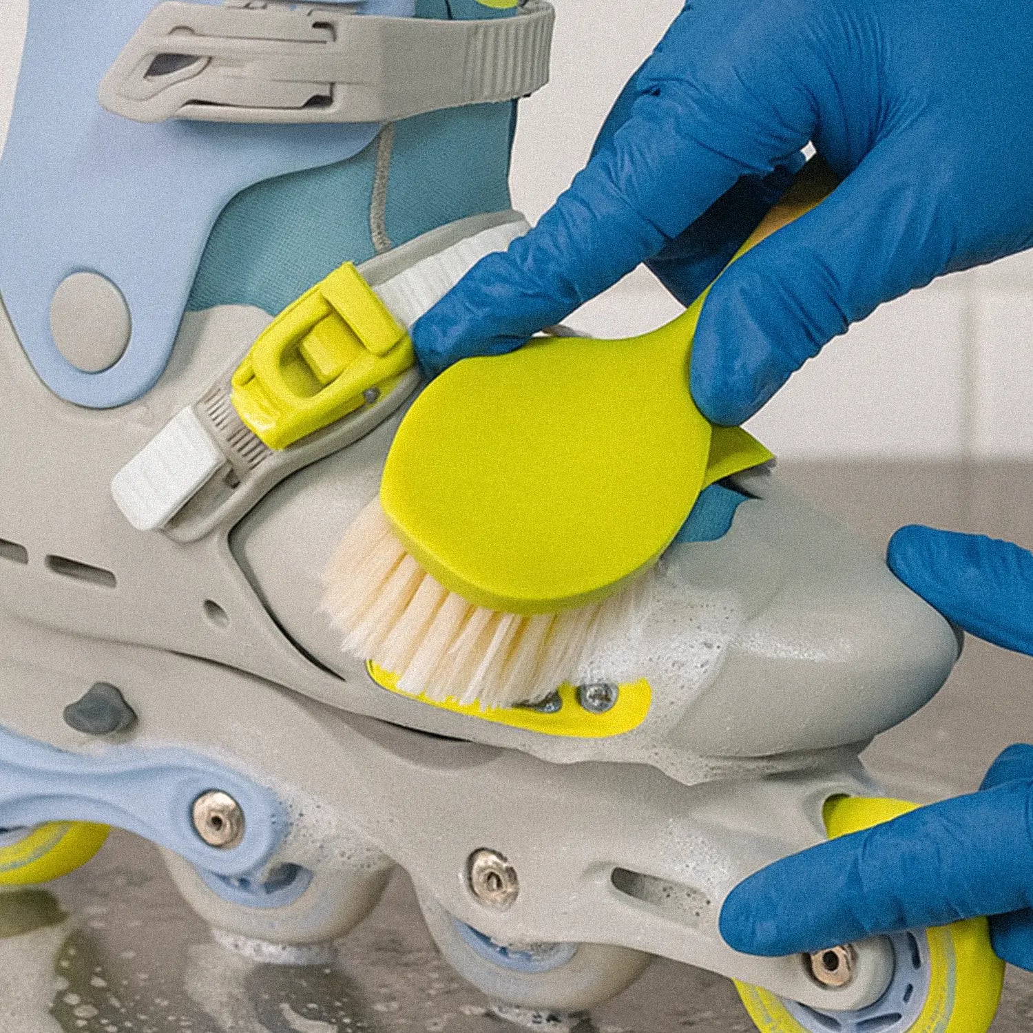 Person cleaning a pair of roller skates with a brush and soap, wearing blue gloves.