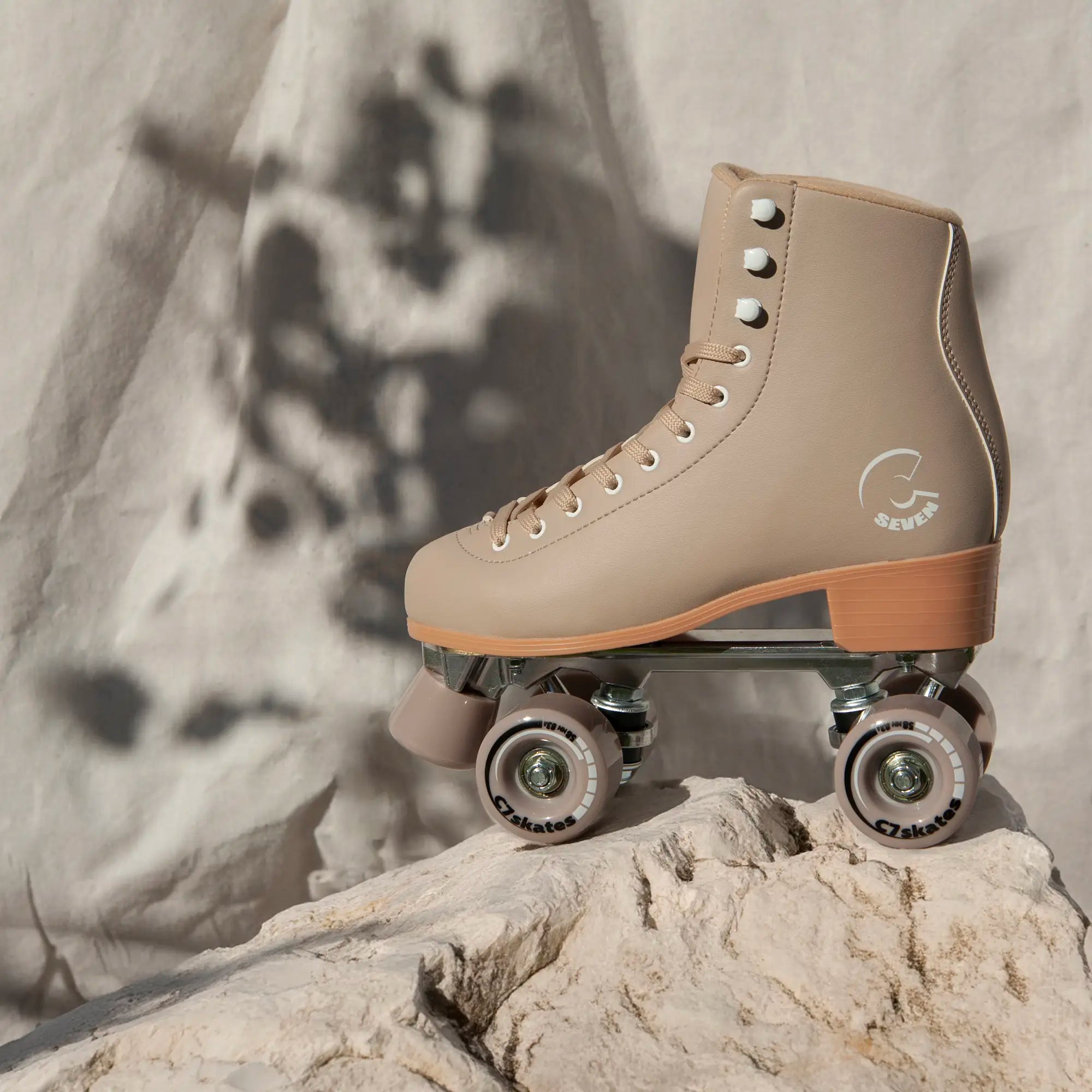 Beige roller skate with brown accents on a rock against a textured wall background