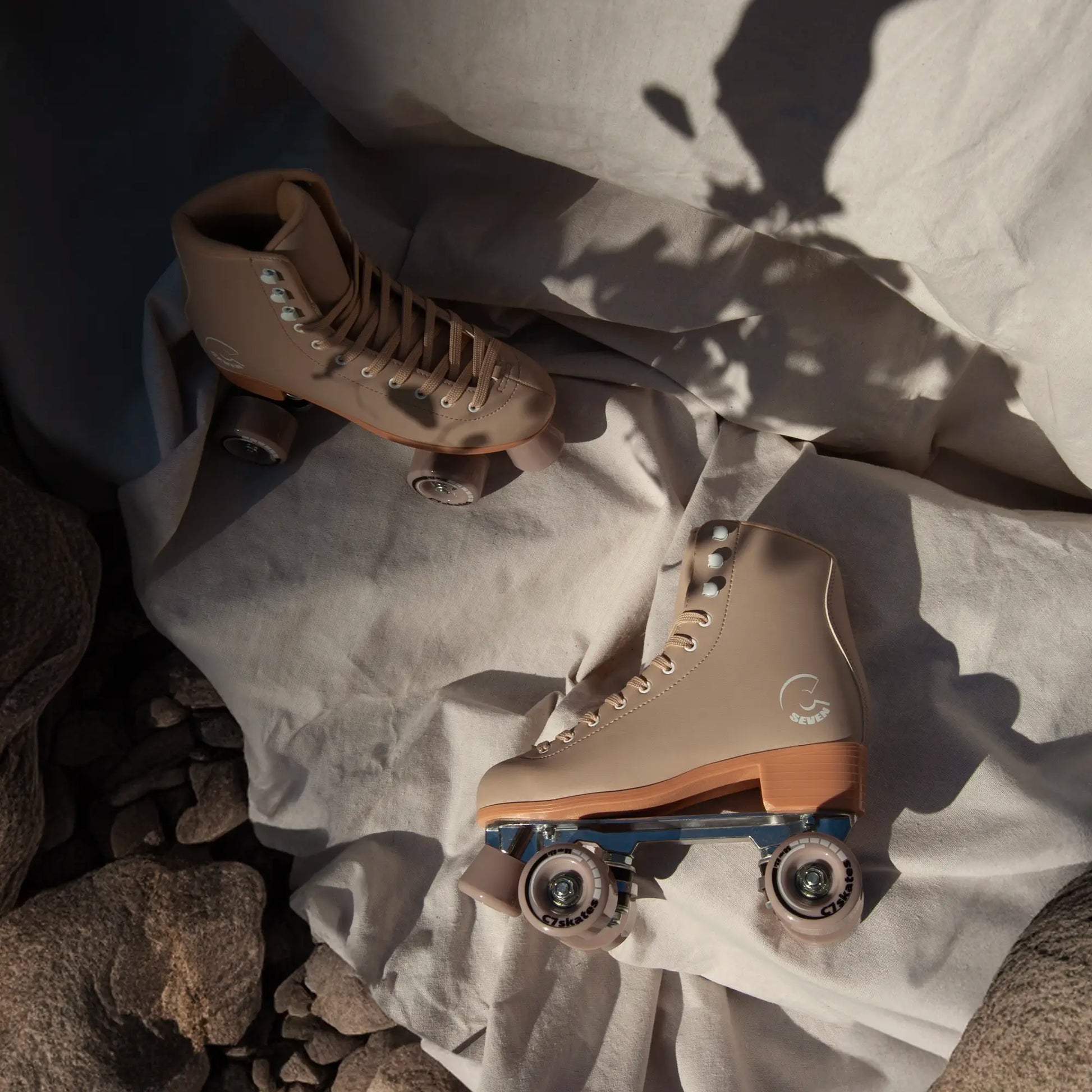 Pair of beige roller skates on a textured surface with rocks and fabric.