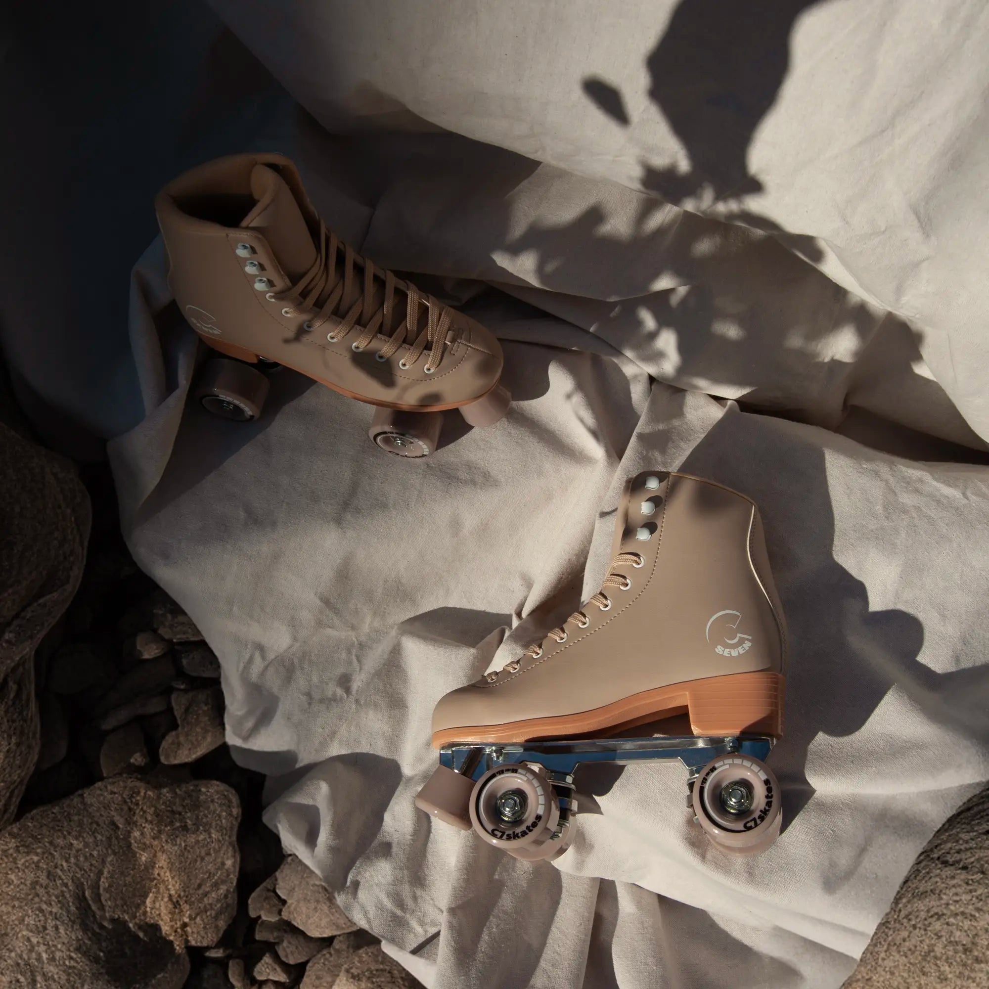 Pair of beige roller skates on a textured surface with rocks and fabric.