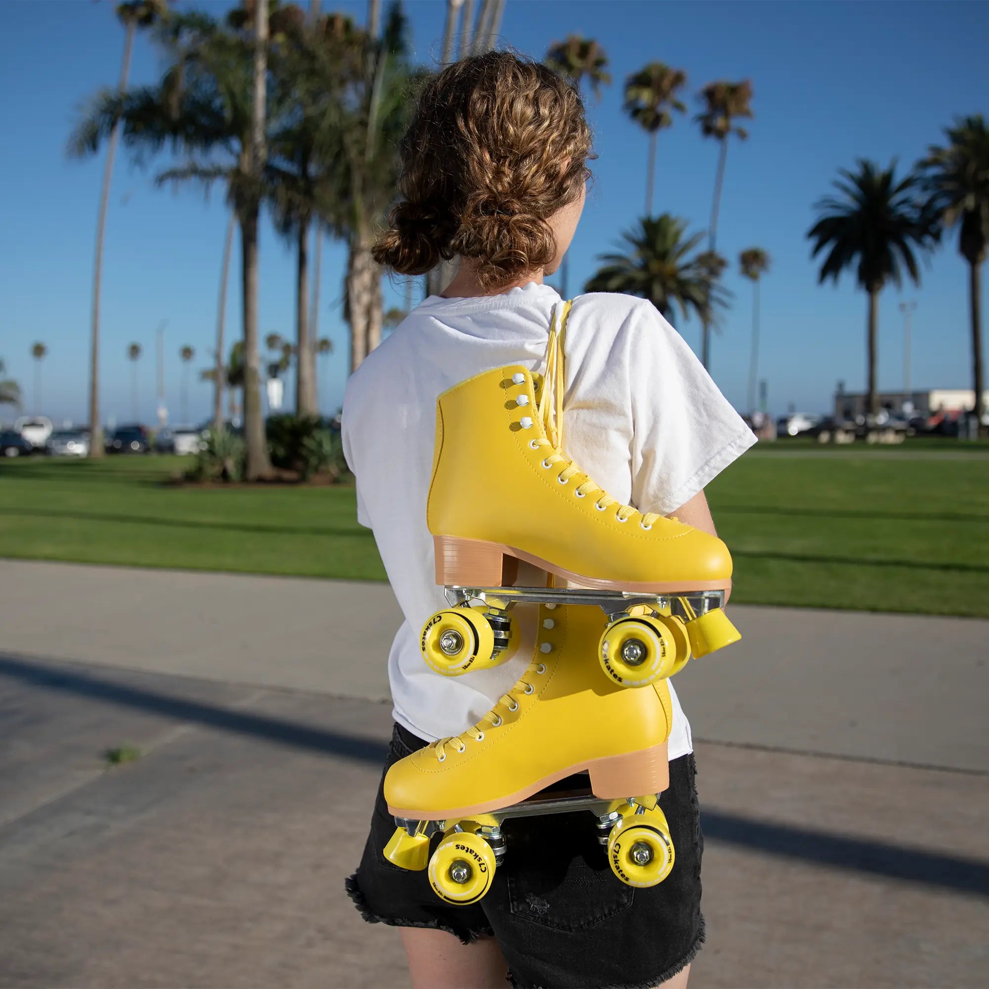 Person holding a yellow roller skate in an outdoor setting with palm trees.