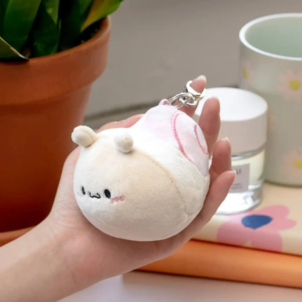 Plush keychain held in a hand with a potted plant and container in the background